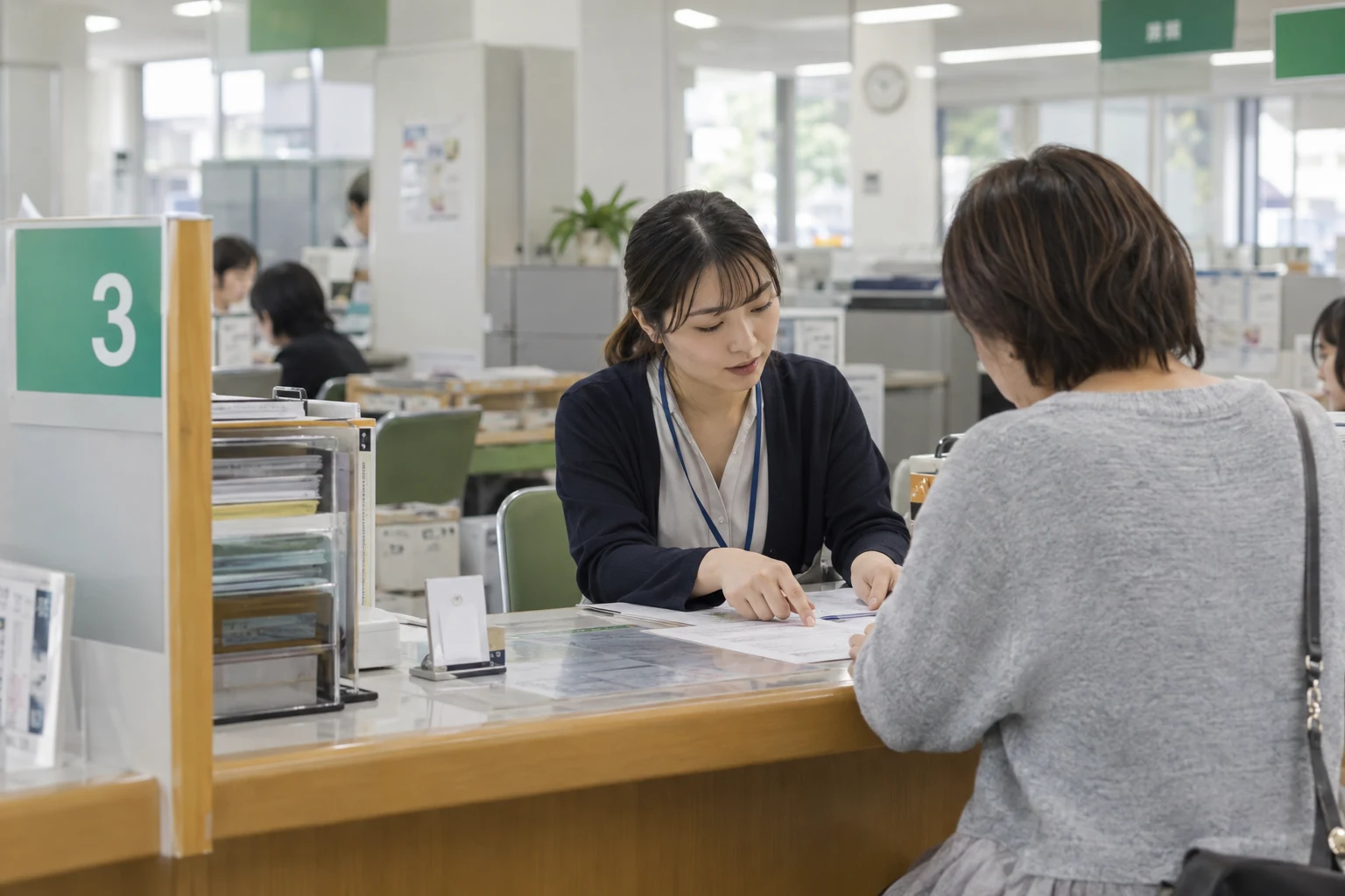 市役所の窓口で職員が来庁者へ手続き書類を案内している様子